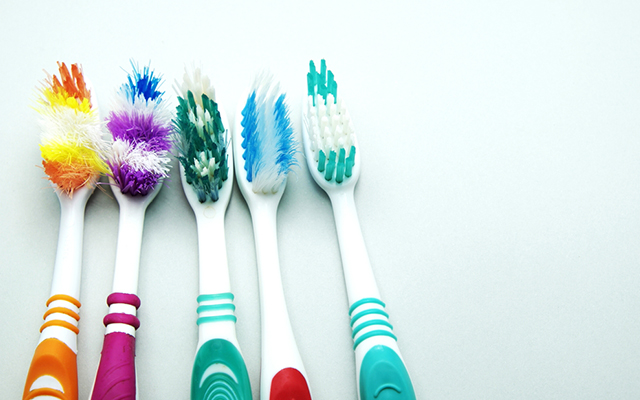 Fünf bunte Zahnbürsten mit abgenutzten Borsten auf weißem Hintergrund, geeignet für Reinigung.